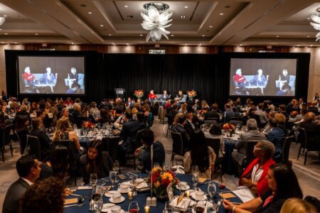 A large number of people sit around circular tables at a gala dinner.