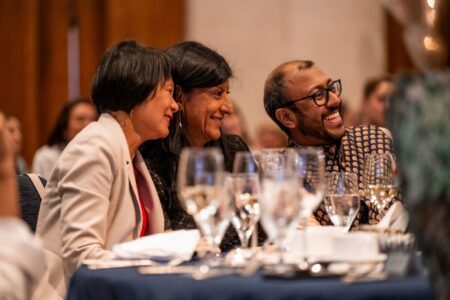 Three people in profile smile to a camera outside of the image.